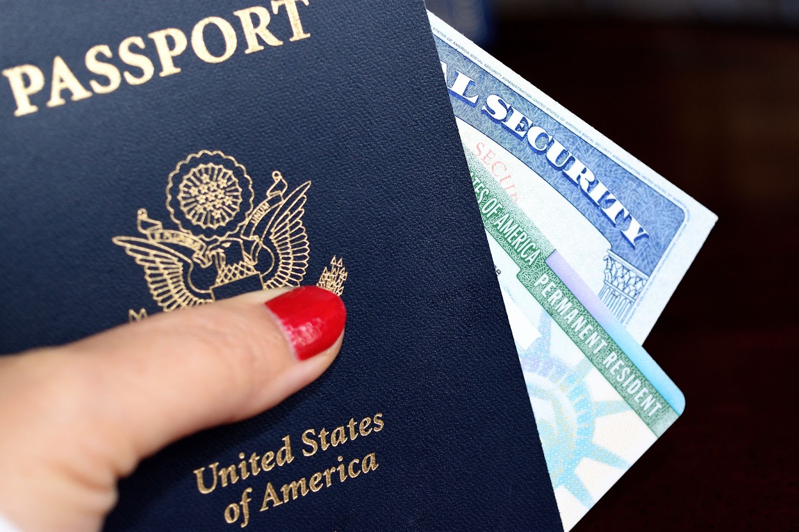 A woman's hand with red nail polish holding a passport and other legal documents for traveling