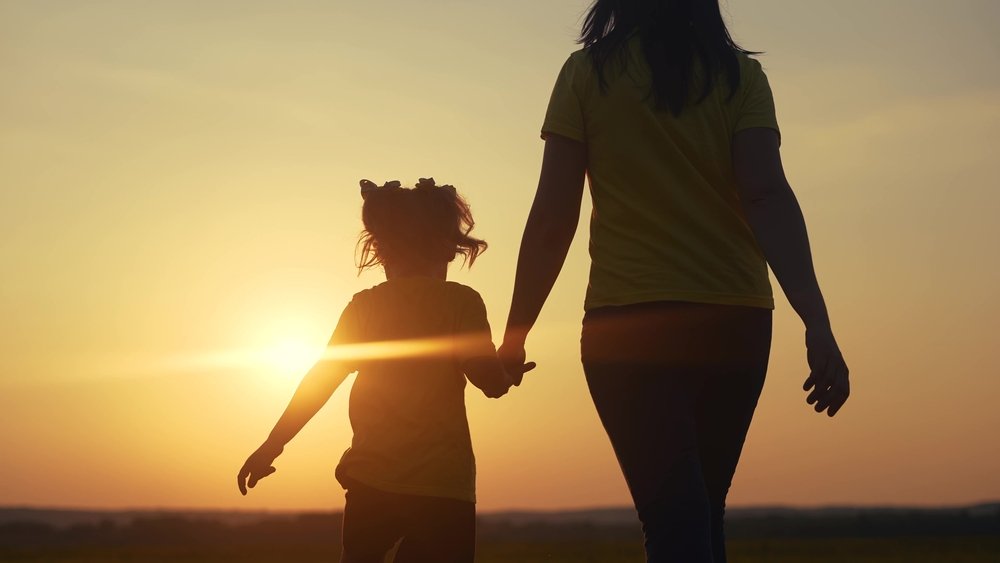 mom and daughter walking into the sunset
