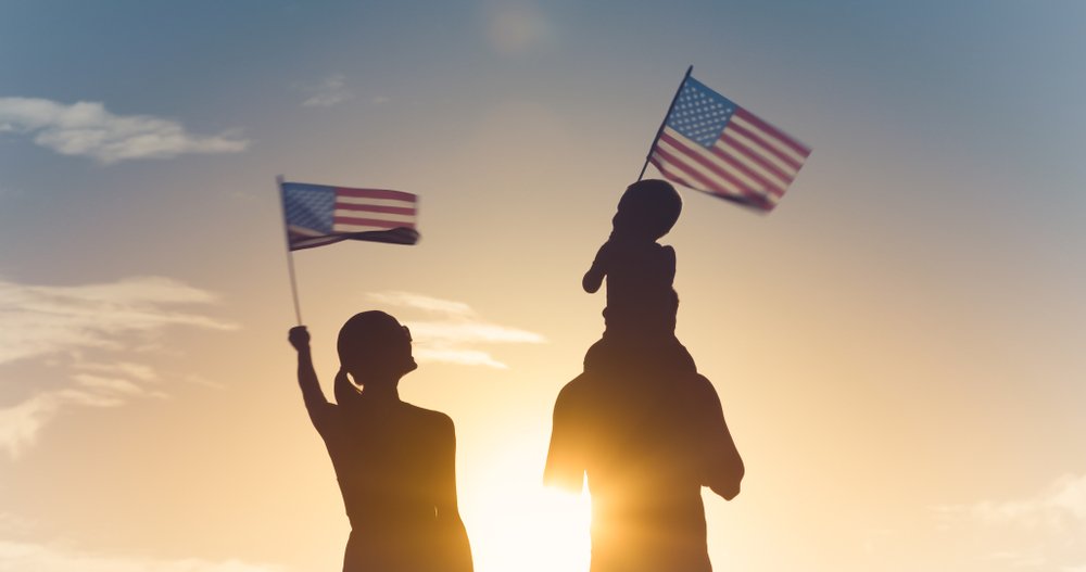 family standing in front of the sunset holding American flags